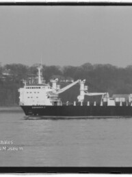 Schwarz-weiß-Foto eines Frachtschiffs mit zwei Ladekränen, das auf ruhigem Wasser vor einem bewaldeten Ufer fährt; links unten Logo und Schriftzug des Internationalen Maritimen Museums Hamburg.
