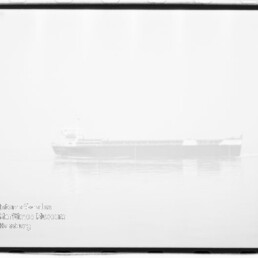 Schwarzweiß-Hochkontrastfoto eines Fracht-/Massengutfrachters, schwach sichtbar und fast überbelichtet, ruhig auf spiegelglattem Meer mit leichter Spiegelung, filmischer Rahmen und Stempel/Wasserzeichen unten links.