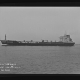 Schwarz-weiß-Fotografie eines langen Tankschiffs mit dem Namen CONGER an der Bordwand, das ruhig auf der See vor flachem Horizont fährt; im unteren linken Bildbereich das Logo und der Schriftzug des Internationalen Maritimen Museums Hamburg.