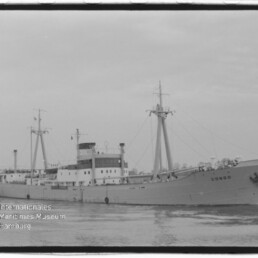 Schwarzweiß-Fotografie eines Frachtschiffs mit dem Namen CONGO am Bug, mittschiffs liegendem Aufbau, zwei Lade-Masten mit Tauwerken und ruhiger Wasseroberfläche, Museumswasserzeichen unten links.
