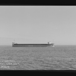 Schwarz-weiß-Foto eines langen Frachtschiffs mit der auf dem Rumpf lesbaren Aufschrift CON-RO, das ruhig auf dem Meer vor flachem Horizont fährt; linke untere Ecke zeigt das Wasserzeichen des Internationalen Maritimen Museums Hamburg.