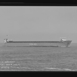 Schwarzweißaufnahme eines langen Frachtschiffs mit der Aufschrift CON-RO am Rumpf, das seitlich auf ruhiger See fährt; Filmrand und Wasserzeichen des Internationalen Maritimen Museums Hamburg sind im Bild sichtbar.