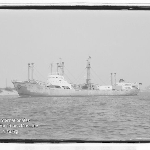 Schwarzweiß-Fotografie eines Frachtschiffs in ruhigem Wasser, seitliche Ansicht mit mehreren Masten und Ladebäumen, Industrieanlagen am Ufer im Hintergrund und Museumslogo „Internationales Maritimes Museum Hamburg“ unten links.