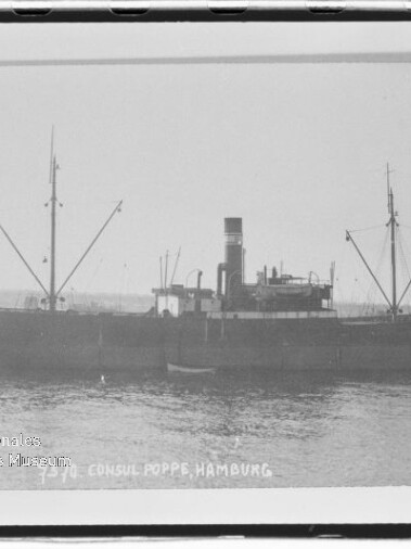 Seitenansicht eines historischen Frachtdampfers mit mittigem Schornstein und zwei Masten, ruhig auf dem Wasser liegend; Schwarzweißfoto mit weißem Rand und der Beschriftung 