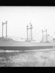 Schwarzweißaufnahme eines Frachtschiffs mit dem Namen CONTINENT, sichtbar sind mehrere Ladebäume, Aufbauten und Bugwellen, im Bild unten links das Wasserzeichen des Internationalen Maritimen Museums Hamburg.
