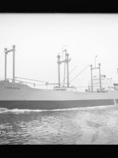 Schwarzweißaufnahme eines Frachtschiffs mit dem Namen CONTINENT, sichtbar sind mehrere Ladebäume, Aufbauten und Bugwellen, im Bild unten links das Wasserzeichen des Internationalen Maritimen Museums Hamburg.