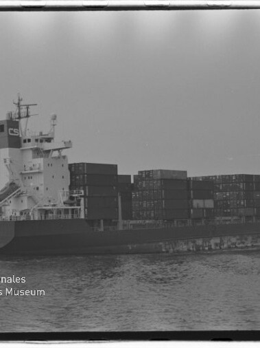Schwarzweiß-Foto eines Containerschiffs (Contship Barcelona) mit gestapelten Containern, das auf ruhiger See fährt, mit Wasserzeichen des Internationalen Maritimen Museums Hamburg unten links.