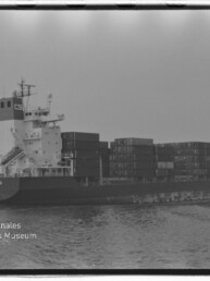 Schwarzweiß-Foto eines beladenen Containerschiffs auf ruhiger See mit mehreren gestapelten Seecontainern, sichtbarem Filmrahmen und Wasserzeichen des Internationalen Maritimen Museums Hamburg unten links.