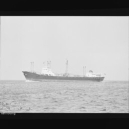 Schwarzweiß-Seitenansicht eines Frachtschiffs auf ruhigem Meer vor hellem Himmel, eingerahmt von Filmrand mit Markierungen und Wasserzeichen 'Internationales Maritimes Museum Hamburg' unten links.