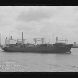 Schwarzweiß-Aufnahme eines Frachtschiffs namens Consequence mit Ladekränen, das auf ruhigem Wasser vor einer industriellen Hafen-Kulisse mit Fabrikschloten fährt.