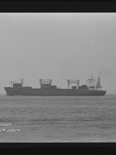 Schwarzweiß-Foto eines Containerschiffs in Seitenansicht auf ruhiger See, sichtbar sind mehrere Ladekräne auf dem Deck, der Filmrand mit Aufdruck 'AGFAPAN 100' und ein Wasserzeichen des Internationalen Maritimen Museums Hamburg im Bild