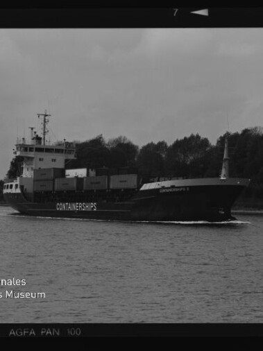 Schwarz-weiß-Foto eines Containerschiffs mit dem Schriftzug CONTAINERSHIPS, beladen mit Containern und fahrend auf ruhigem Wasser vor einer baumbestandenen Uferlinie; Filmkanten und das Logo des Internationalen Maritimen Museums Hamburg sind im Bildrand sichtbar.