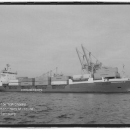 Schwarzweißbild eines beladenen Containerschiffs mit dem Schriftzug „CONTAINERSHIPS“, das im Hafen neben großen Hafenkranen liegt; unten links das Logo des Internationalen Maritimen Museums Hamburg.