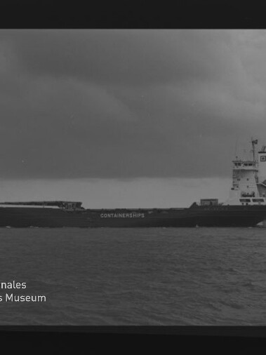 Schwarzweiß-Aufnahme eines Containerschiffs in Seitenansicht auf ruhiger See unter bewölktem Himmel, mit rückwärtigem Aufbauturm, dem Schriftzug CONTAINERSHIPS am Rumpf sowie sichtbarem Filmrand und Wasserzeichen des Internationalen Maritimen Museums Hamburg