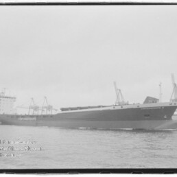 Schwarzweißfoto eines großen Containerschiffs mit dem Schriftzug ‚CONTAINERSHIPS‘, das vor einem Industriehafen mit Ladekränen auf ruhiger See vorbeifährt.