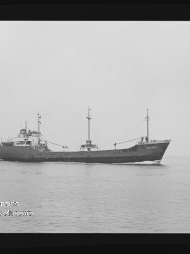 Schwarzweißaufnahme eines Frachtschiffs in Seitenansicht, das ruhig über das Meer fährt; das Bild zeigt einen breiten Filmrand und ein Wasserzeichen des Internationalen Maritimen Museums Hamburg in der unteren linken Ecke.