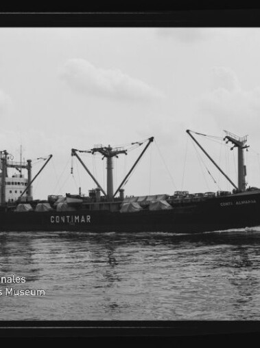 Schwarzweißaufnahme eines Frachtschiffs mit der Aufschrift CONTIMAR, mehreren Ladebäumen und planenbedeckter Decksladung, auf ruhiger See unter bedecktem Himmel; Wasserzeichen des Internationalen Maritimen Museums Hamburg unten links.