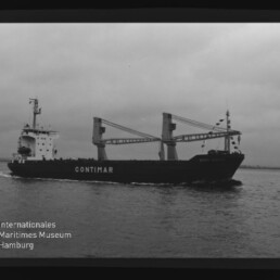 Schwarzweißaufnahme eines Frachtschiffs mit der Aufschrift CONTIMAR und zwei großen Ladekränen, das bei bedecktem Himmel auf ruhiger See fährt; links unten Logo des Internationalen Maritimen Museums Hamburg.