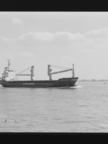 Schwarzweißaufnahme eines Frachtschiffs mit der Aufschrift CONTIMAR und zwei Ladekränen, das auf ruhiger See vor flachem Horizont mit vereinzelten Booten fährt; Filmnegativrand und Wasserzeichen des Internationalen Maritimen Museums Hamburg sichtbar.