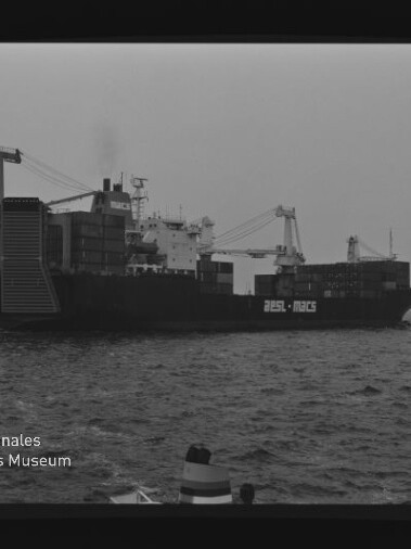 Schwarzweiß-Seitenansicht eines beladenen Containerschiffs mit Ladekränen und gestapelten Containern auf ruhiger See; Wasserzeichen des Internationalen Maritimen Museums Hamburg unten links.