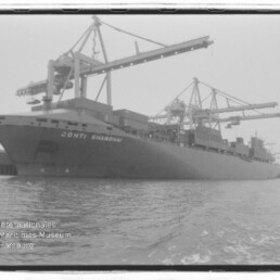 Schwarzweißaufnahme eines großen Containerschiffs mit der Aufschrift CONTI SHANGHAI, am Hafen unter mehreren hohen Ladekränen liegend, mit Wasser im Vordergrund und Museumswasserzeichen unten links.