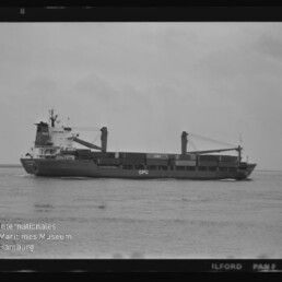 Schwarzweiß-Fotografie eines Frachtschiffs in Seitenansicht auf ruhiger See mit zwei Ladekränen und der Aufschrift „CPC“, sichtbar sind Filmrand und Wasserzeichen des Internationalen Maritimen Museums Hamburg.