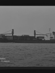 Schwarzweiß-Seitenansicht eines beladenen Containerschiffs mit zwei Ladekränen und achterlicher Aufbauten auf ruhiger See, umgeben von schwarzem Filmrand mit Kodak-Schriftzug und Wasserzeichen des Internationalen Maritimen Museums Hamburg.
