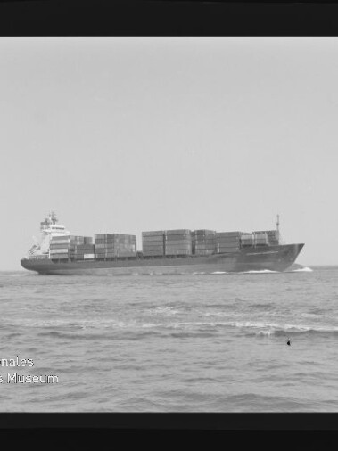Schwarzweißaufnahme eines beladenen Containerschiffs auf ruhiger See, seitliche Ansicht mit gestapelten Containern sowie sichtbarem Negativrahmen und Wasserzeichen des Internationalen Maritimen Museums Hamburg