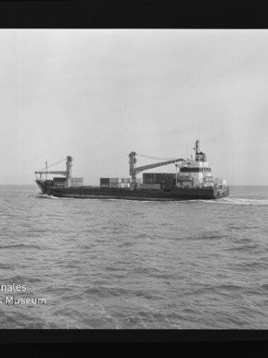 Schwarzweißaufnahme eines Frachtschiffs mit zwei Ladekränen und gestapelten Containern auf ruhiger See; Negativfilmrand mit der Aufschrift KODAK FXP und Wasserzeichen des Internationalen Maritimen Museums Hamburg sichtbar.