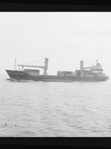 Schwarzweiß-Fotografie eines Frachtschiffs in Seitenansicht mit zwei Ladekränen und mehreren Containern an Deck, fahrend auf ruhiger See, umgeben von einem Filmnegativrand mit der Aufschrift ‚KODAK FXP 6040‘ und Wasserzeichen des Internationalen Maritimen Museums Hamburg.