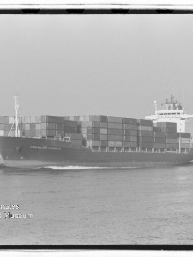 Schwarzweißaufnahme eines großen Containerschiffs, beladen mit mehrfach übereinander gestapelten Ladecontainern und mit sichtbarer Brücke, das auf ruhigem Meer fährt; links unten Logo des Internationalen Maritimen Museums Hamburg.