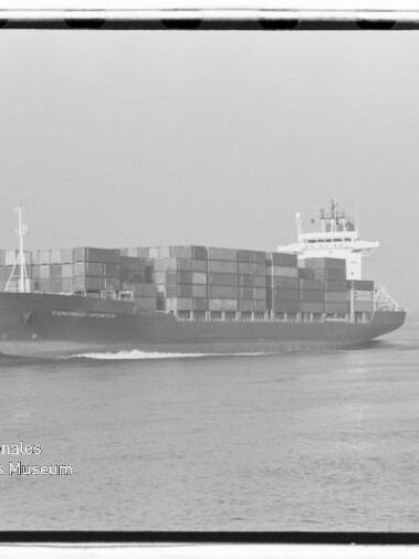 Schwarzweißaufnahme eines beladenen Containerschiffs mit mehreren Reihen hoch gestapelter Container, das ruhig auf dem Wasser fährt; unten links eingeblendetes Logo und Schriftzug des Internationalen Maritimen Museums Hamburg.
