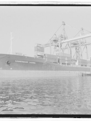 Containerschiff CONTSHIP JORK liegt am Kai eines Hafens unter großen Brückenkränen, gestapelte Container an Deck und ruhiges Wasser im Vordergrund; Stempel Internationales Maritimes Museum Hamburg unten links.