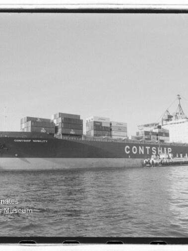 Großes Containerschiff mit der Aufschrift CONTSHIP, beladen mit Containern und am Kai liegend, davor ruhiges Wasser und im Hintergrund Hafenkräne; Wasserzeichen des Internationalen Maritimen Museums Hamburg in der unteren linken Ecke.
