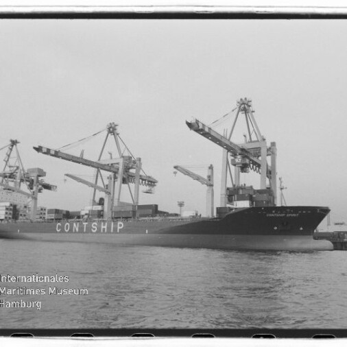 Schwarzweißaufnahme eines großen Containerschiffs mit der Aufschrift CONTSHIP, das am Hafen unter mehreren Containerkränen liegt; Wasser im Vordergrund und das Logo des Internationalen Maritimen Museums Hamburg unten links.