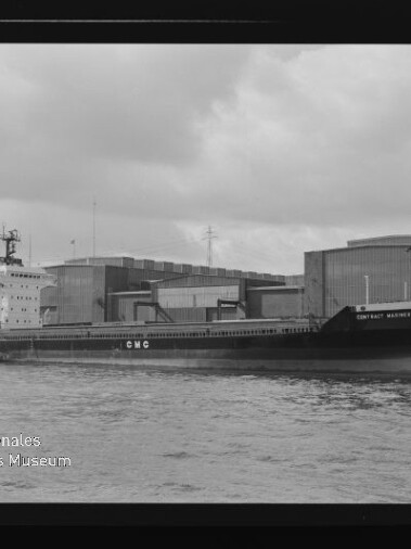 Schwarzweißaufnahme eines am Kai liegenden Frachtschiffs mit der Aufschrift „CMC“, im Hintergrund Lagerhallen und ein Kran, im Vordergrund Wasser sowie sichtbarer Filmrand und Wasserzeichen des Internationalen Maritimen Museums Hamburg.