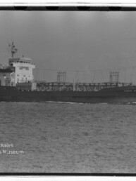 Schwarzweiß-Seitenansicht eines mittelgroßen Tankschiffs mit Namen „Coral Fernandez“ auf ruhiger See, sichtbare Decksleitungen und Brücke links, mit Filmrand und Wasserzeichen des Internationalen Maritimen Museums Hamburg unten links.
