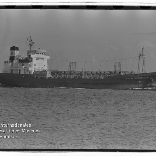 Schwarzweiß-Seitenansicht eines mittelgroßen Tankschiffs mit Namen „Coral Fernandez“ auf ruhiger See, sichtbare Decksleitungen und Brücke links, mit Filmrand und Wasserzeichen des Internationalen Maritimen Museums Hamburg unten links.