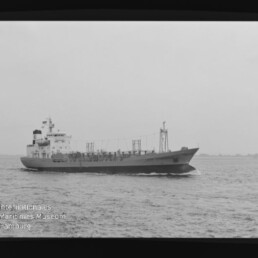 Schwarzweiß-Seitenansicht eines Tankschiffs auf ruhiger See mit Aufbauten achtern und sichtbaren Rohrleitungen auf dem Deck, weiter Horizont im Hintergrund und einem weißen Logo des Internationalen Maritimen Museums Hamburg unten links.