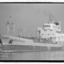 Schwarzweiß-Seitenansicht des Frachtschiffs Coral Essberger auf ruhigem Wasser mit komplexen Decksaufbauten und Rohrleitungen; links unten Logo und Schriftzug 'Internationales Maritimes Museum Hamburg'.