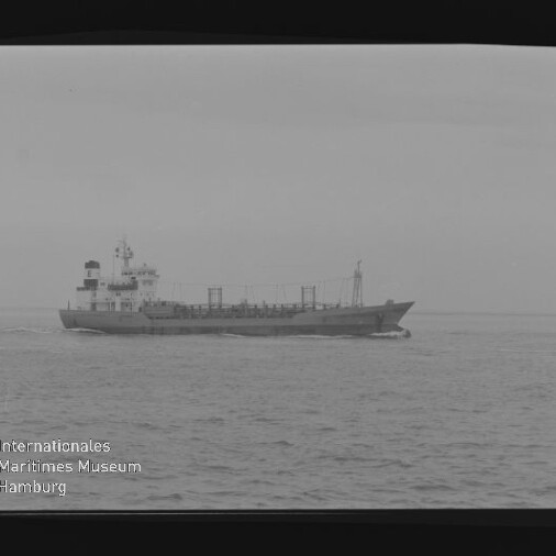Schwarzweiß-Foto eines Frachtschiffs in Seitenansicht auf ruhiger See, mit Aufbau und Masten, Filmbandrahmen und Wasserzeichen des Internationalen Maritimen Museums Hamburg links unten.