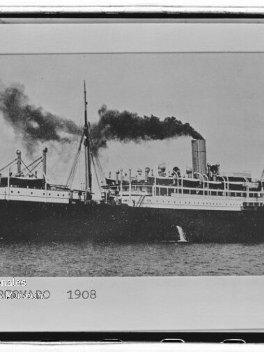 Schwarzweiß-Foto eines großen Dampfschiffs auf ruhiger See von 1908, mit mittigem Schornstein, dunklem Rauch, mehreren Masten und der Jahresangabe „1908“ unten im Bild.
