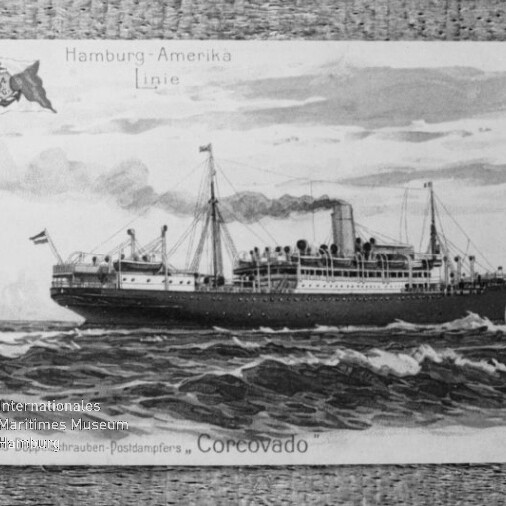 Schwarzweiß-Postkarte mit einer Illustration des Dampfschiffs „Corcovado“ der Hamburg‑Amerika Linie, das mit rauchendem Schornstein und Masten durch bewegte See fährt; die Karte wird an den oberen Ecken gehalten und trägt ein Museumswasserzeichen.