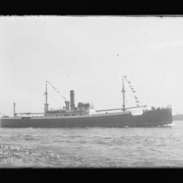 Schwarzweiß-Seitenansicht eines historischen Dampfschiffs mit mittigem Schornstein und beflaggten Masten auf ruhiger See, links unten Wasserzeichen des Internationalen Maritimen Museums Hamburg.