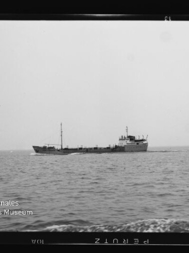 Schwarz-weiß-Foto eines mittig positionierten Frachtschiffs auf ruhiger, leicht welliger See, mit hellem, wolkenlosem Himmel und dem Wasserzeichen „Internationales Maritimes Museum Hamburg“ unten links.