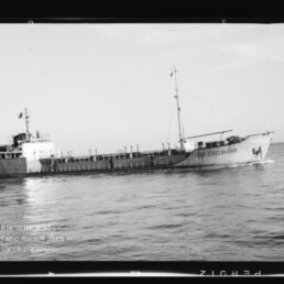 Schwarzweiß-Foto eines Frachtschiffs mit dem Namen Cabo Eckelmann, seitliche Ansicht bei ruhiger See mit Aufbauten achtern, Mast über dem Laderaum und Museumswasserzeichen unten links.