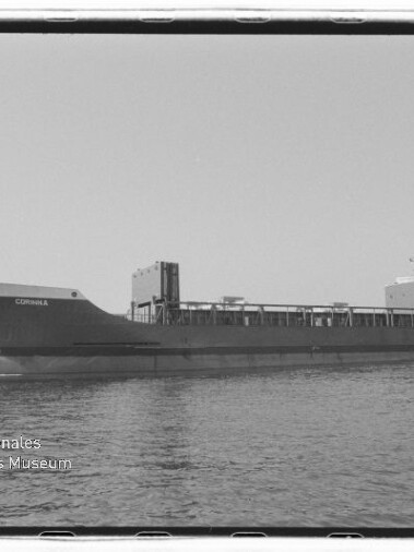 Schwarzweißaufnahme eines seitlich gezeigten Frachtschiffs namens 'CORINNA' im Hafen vor Ladekränen und einem Flutlichtmast, mit ruhiger Wasserfläche und dem Logo des Internationalen Maritimen Museums Hamburg links unten.