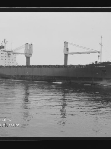 Großes Frachtschiff namens CORONA mit zwei markanten Deckskranen und achterlichem Aufbauten, ruhig auf spiegelglattem Wasser fotografiert, umgeben von sichtbarem Filmrand und Museumswasserzeichen unten links.