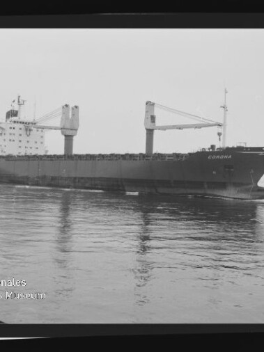 Schwarzweißaufnahme eines Frachtschiffs namens Corona in Seitenansicht auf ruhigem Wasser, mit zwei großen Ladekränen auf dem Deck, sichtbarem Filmrand und der Beschriftung AGFA PAN 100 am rechten Bildrand