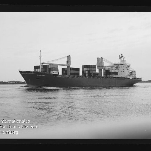 Schwarzweiß-Foto eines Containerschiffs, das mit gestapelten Containerblöcken und zwei Ladekränen über ruhigem Wasser fährt, mit Wasserreflexionen im Vordergrund und einem Wasserzeichen des Internationalen Maritimen Museums Hamburg links unten.